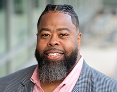 Marcus Young is an African American man wearing a pink shirt and gray blazer