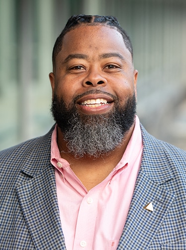 Marcus Young is an African American man wearing a gray suit jacket and pink shirt