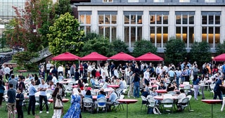 grassy courtyard with food tents and people seated at tables or milling about