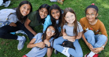 Six smiling students seated on the grass