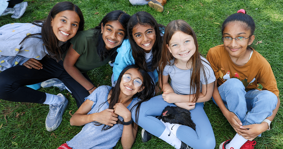 Six smiling students seated on the grass