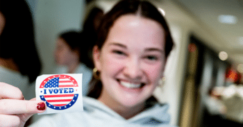 Female student holds an "I voted" sticker.