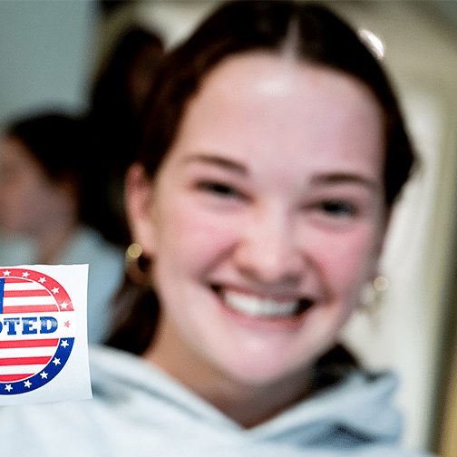 Female student holds an "I voted" sticker.