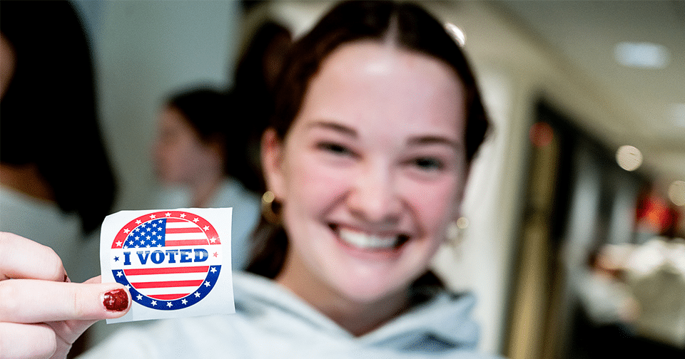 Female student holds an "I voted" sticker.