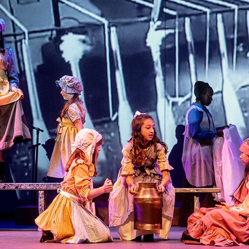 Students on stage performing a play called "Mill Girls"