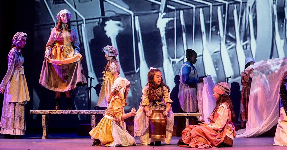 Students on stage performing a play called "Mill Girls"