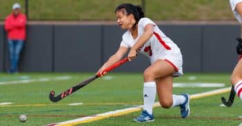 Student-athlete holds a field hockey stick and passes a ball