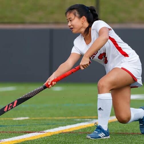 Student-athlete holds a field hockey stick and passes a ball