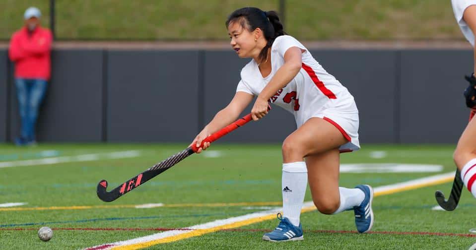 Student-athlete holds a field hockey stick and passes a ball