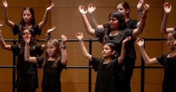 Student vocalists stand to sing with their hands raised high