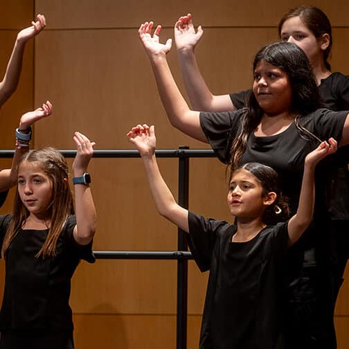 Student vocalists stand to sing with their hands raised high