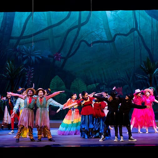 students on stage dancing dressed in colorful costumes