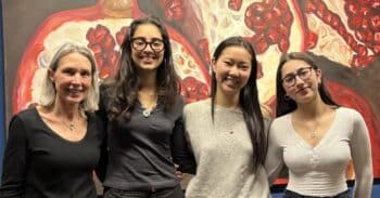 Three alums and a teacher stand in front of a painting of a pomegranate.